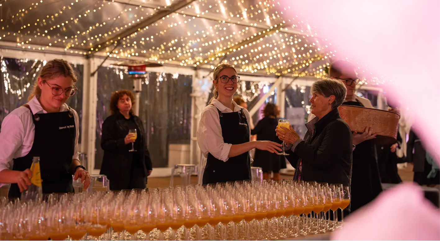 Waitstaff handing a guest a drink under fairy lights at a 60th birthday celebration