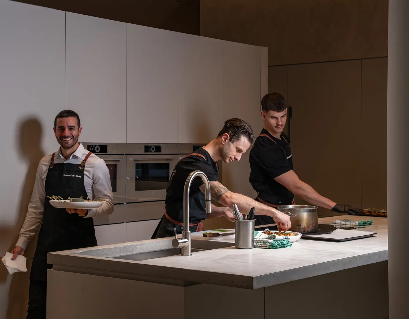 Chefs and a waiter working the kitchen in sequence as event service gets underway