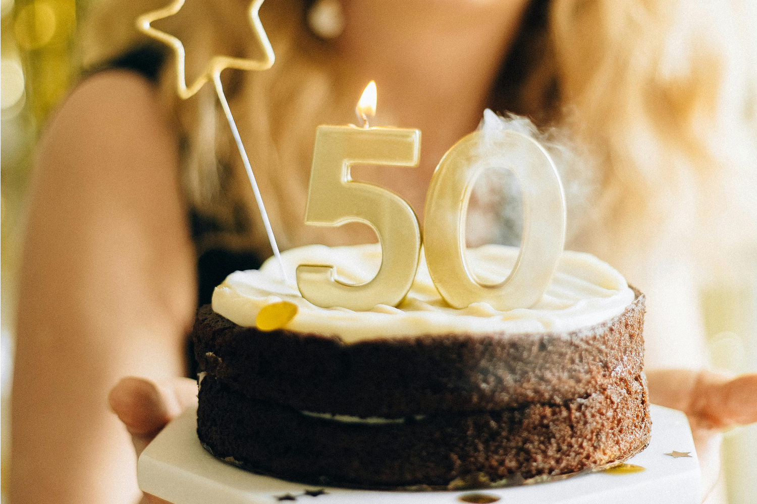 Woman celebrating 50th birthday blowing out candles on cake