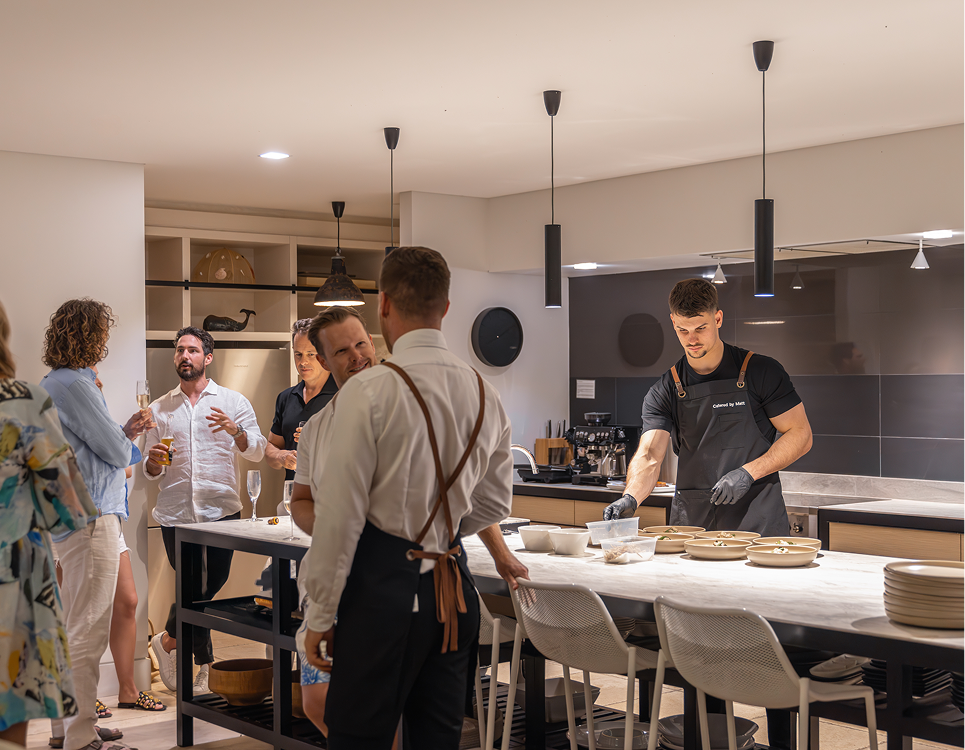 Chef Matt prepares dishes in a warmly lit kitchen, with 20 guests enjoying the event
