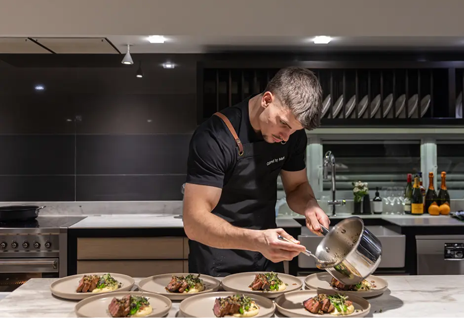 Chef Matt spooning sauce over a row of plated courses at a Penrith event