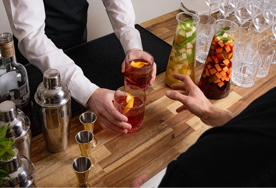 Bar staff handing over cocktails beside infused jugs at a Penrith event