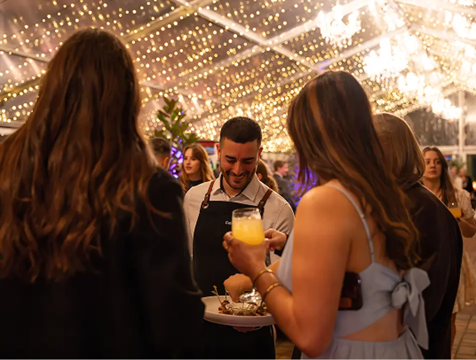 Waiter serving canapés and drinks under fairy lights at a North Shore event
